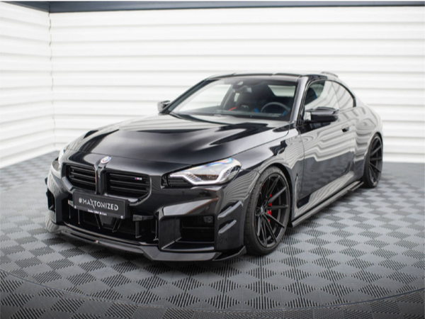 A sleek black sports car is parked on a checkered floor, with the text "#MAXTONIZED" on the front plate, set against a white, ridged background.
