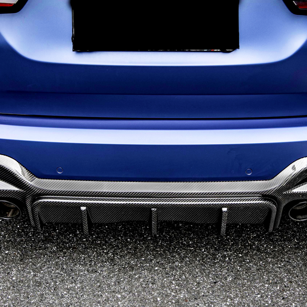 A blue car's rear with a carbon fiber diffuser and four exhaust pipes, parked on an asphalt surface. The license plate area is obscured.