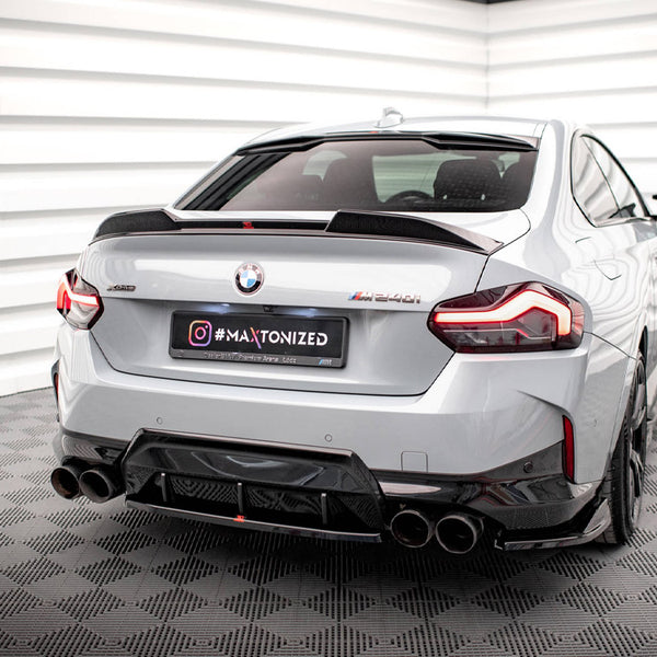 A silver BMW M240i is parked in a white, geometric-patterned room, featuring quad exhausts and elegant taillights. The license plate reads "#MAXTONIZED" with additional text: "Official Premium Partner MAZ 2021."