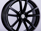 A black car wheel rim with a glossy finish stands upright. The center features a logo with a 