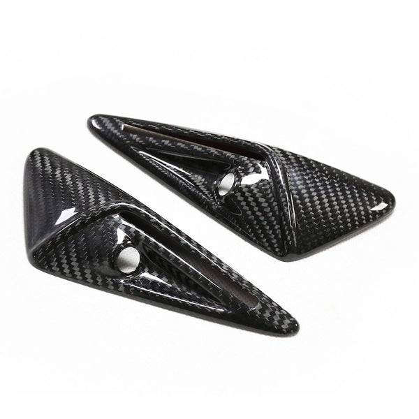 Two carbon fiber, triangular car accessories with polished surfaces and circular cutouts are placed on a plain white background.