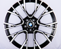 A black and silver alloy wheel features intricate spoke design with a BMW logo at the center, resting against a plain white backdrop.