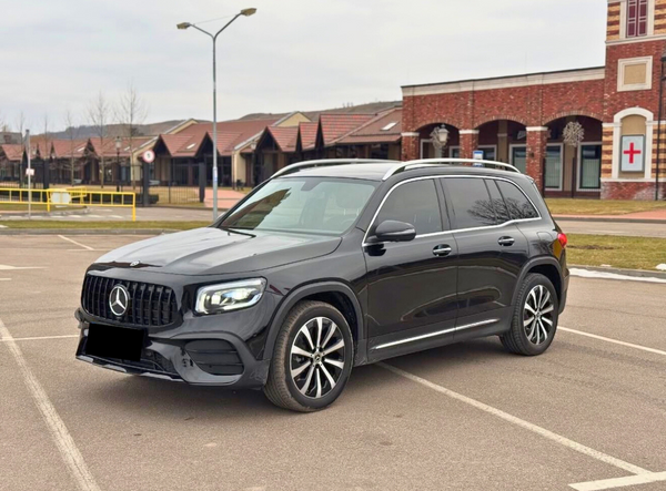A black SUV is parked in an empty lot, surrounded by brick buildings and leafless trees under a cloudy sky. The vehicle features a prominent front grille and sleek design.