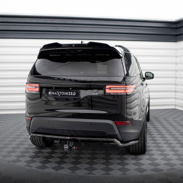 A black SUV is parked in a well-lit, indoor area with patterned flooring. The vehicle's license plate displays "#MAXTONIZED," and its rear lights are illuminated.