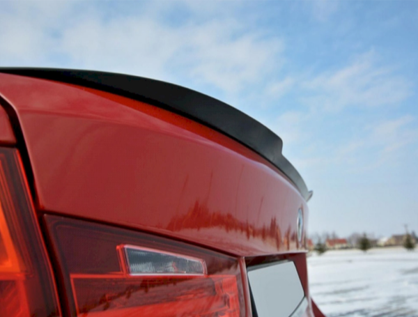 Red car trunk with a small spoiler. The car is stationary on a snow-covered field. The sky is clear with scattered clouds.