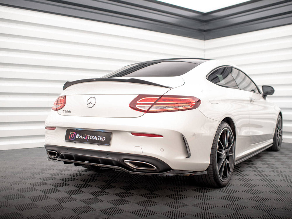 A white Mercedes-Benz C-Class coupe is stationary, displayed in a well-lit showroom with checkered flooring. The license plate reads "#MAXTONIZED."