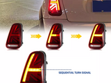 Taillights shaped like the Union Jack display a sequential turn signal action, with arrows indicating activation sequence. Context includes a car’s rear in a nighttime urban setting. Text: 