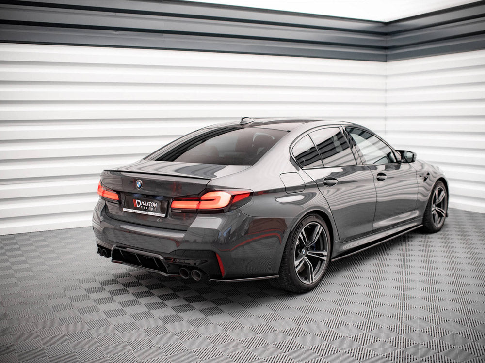 A sleek gray car is parked, facing away, in a brightly lit, modern showroom with checkered flooring. The license plate reads "MAXTON."