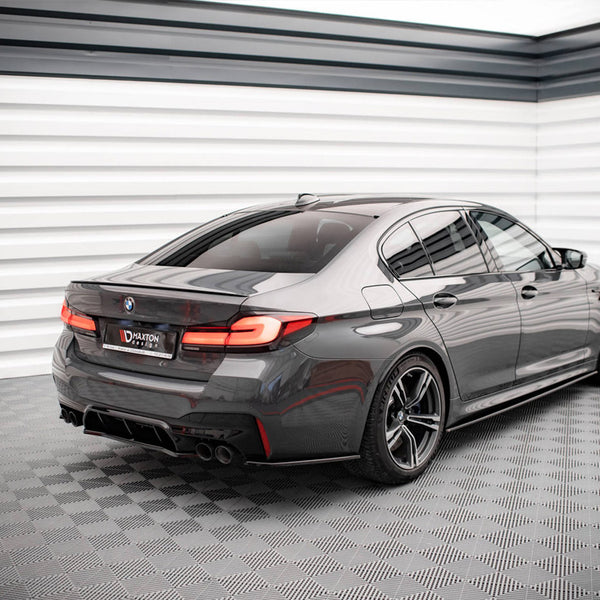 A sleek gray car is parked, facing away, in a brightly lit, modern showroom with checkered flooring. The license plate reads "MAXTON."