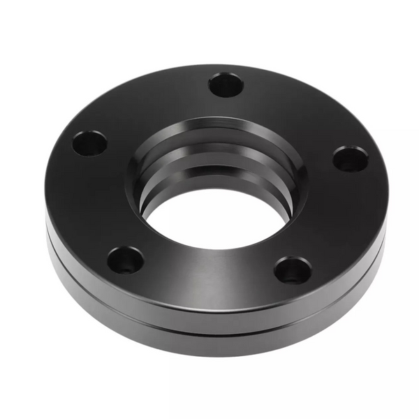 A black metal flange features five bolt holes and a central threaded opening, lying stationary against a plain white background.
