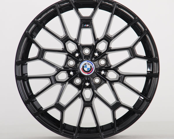 The image shows a black alloy wheel with a complex geometric design, featuring a blue, white, and red BMW logo at the center. The wheel is set against a plain white background.