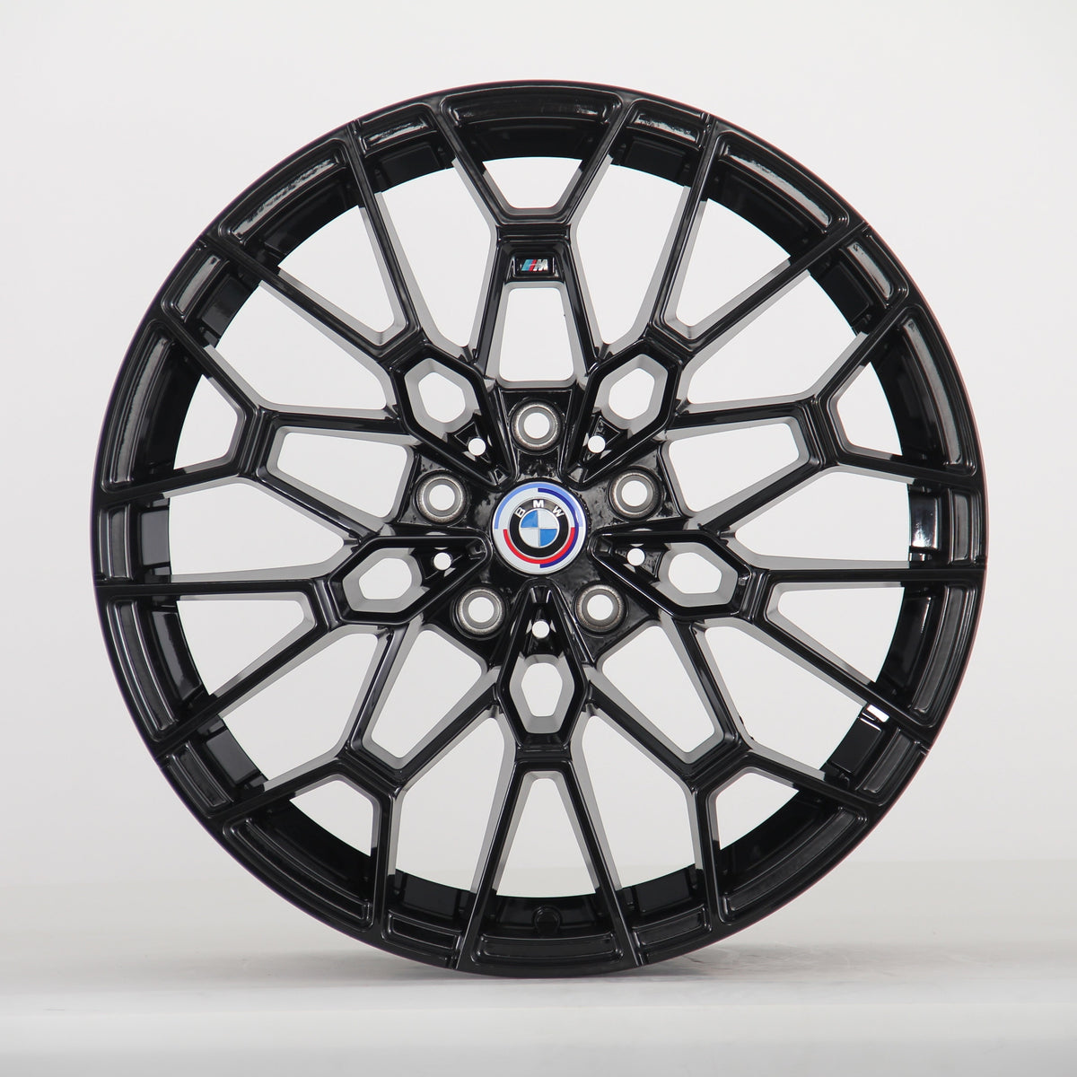 The image shows a black alloy wheel with a complex geometric design, featuring a blue, white, and red BMW logo at the center. The wheel is set against a plain white background.