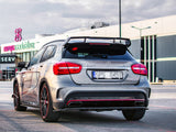 A silver Mercedes-Benz A45 AMG parked in a shopping center lot, featuring spoiler and red accents. Background shows buildings with 