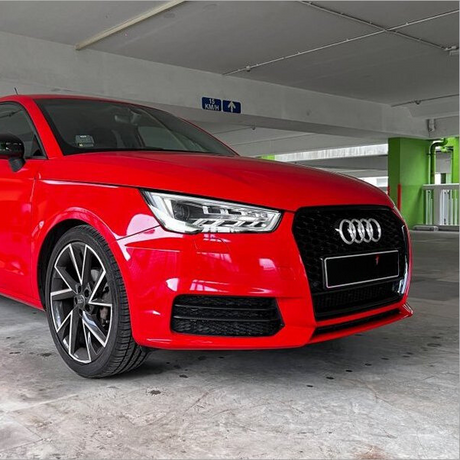 A red car, stationary, with a distinctive front grille and elegant headlights, is parked in a covered parking area. A sign above indicates "15 KM/H" and arrows for direction.