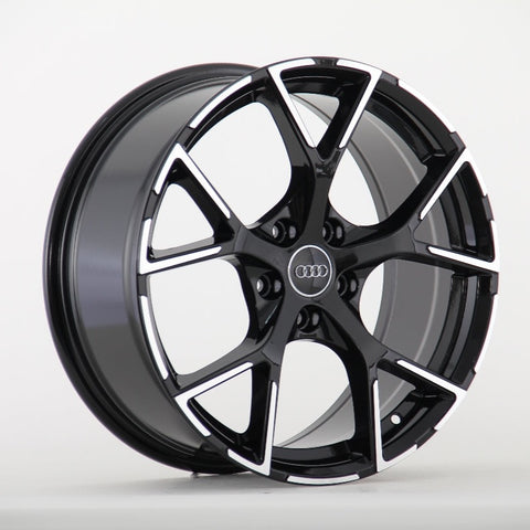 A black and silver Audi wheel rim with a five-spoke design is displayed against a plain white background. The Audi logo is centered on the wheel hub.