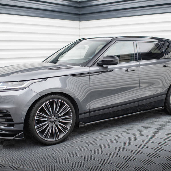 A sleek gray SUV is parked in a modern showroom with textured walls. It's a Range Rover, featuring large alloy wheels and a stylish, streamlined design.