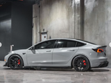 A gray sports car is parked in a sleek, industrial garage with concrete walls and polished floors. It has black wheels and red brake calipers.