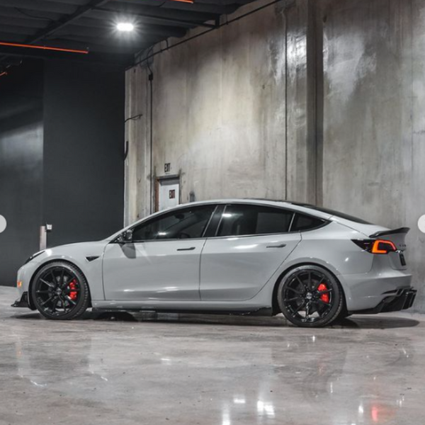A gray sports car is parked in a sleek, industrial garage with concrete walls and polished floors. It has black wheels and red brake calipers.