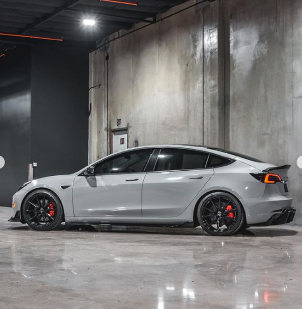 A gray sports car is parked in a sleek, industrial garage with concrete walls and polished floors. It has black wheels and red brake calipers.