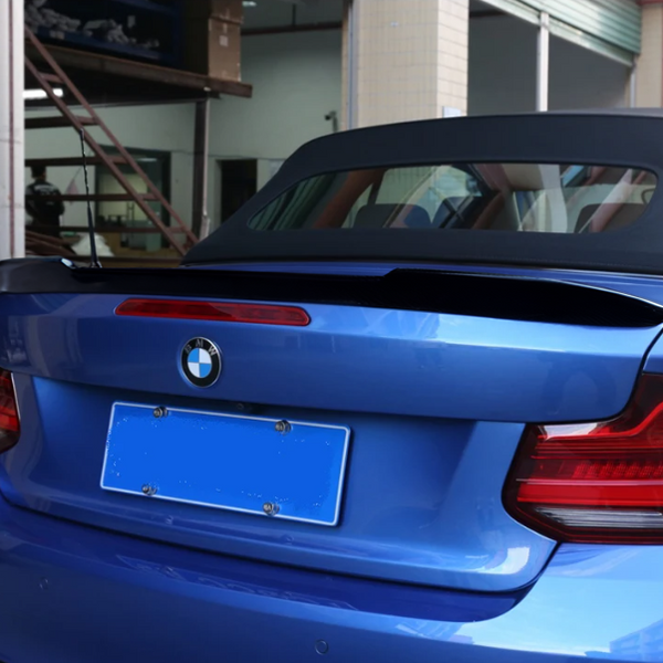 A blue convertible car with the top down is parked in a garage with tiled walls and a staircase. The back features a BMW logo and blurred license plate.
