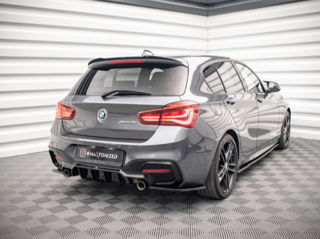 A grey BMW car is parked in a showroom with patterned flooring and white paneled walls. The car has "F21 M" and "maxtonized" written on the back.