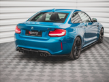 A blue BMW sports car is parked in a showroom with a textured gray floor and white walls. The vehicle features quad exhaust pipes and the text 