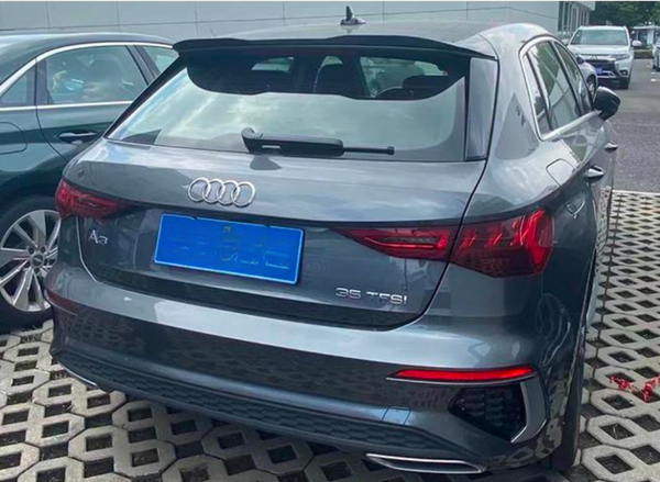 A gray Audi A3 car is parked on a patterned surface, adjacent to another vehicle. Text on the car reads "A3" and "35 TFSI." The weather is overcast.