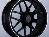 A black alloy wheel with a multi-spoke design, featuring a Mercedes emblem in the center and an 