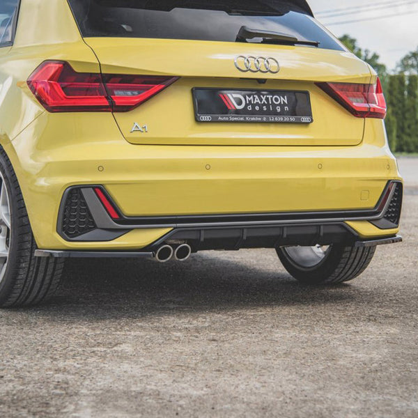 A yellow car is parked on a concrete surface, showcasing its rear view with a visible dual exhaust. The number plate reads "MAXTON Design Auto Special Kraków tel. 12 639 30 50."