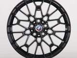 A black alloy wheel with intricate spokes is displayed, featuring a central BMW emblem. The wheel stands vertically against a plain white background.