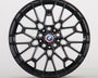 A black alloy wheel with intricate spokes is displayed, featuring a central BMW emblem. The wheel stands vertically against a plain white background.