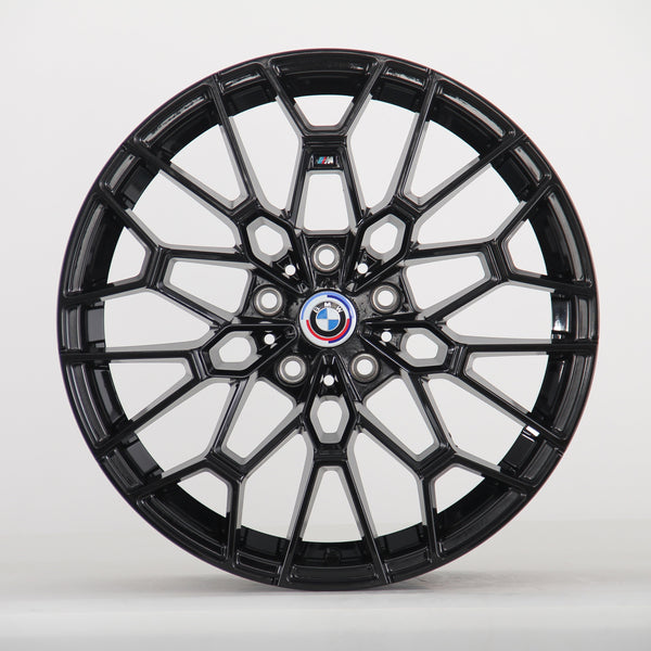 A black alloy wheel with intricate spokes is displayed, featuring a central BMW emblem. The wheel stands vertically against a plain white background.