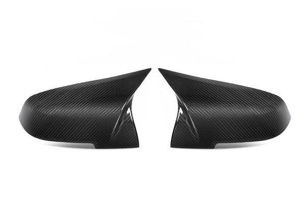 Two carbon fiber side mirror covers are placed symmetrically, angled towards each other, against a plain white background, highlighting their sleek, aerodynamic design and glossy texture.