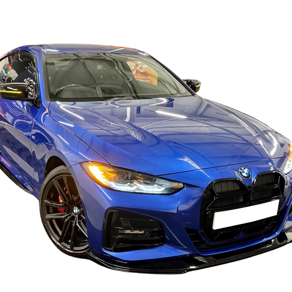 A blue sports car with headlights on is parked in a showroom, reflecting overhead lights. The environment's reflections highlight the vehicle's sleek, aerodynamic design.