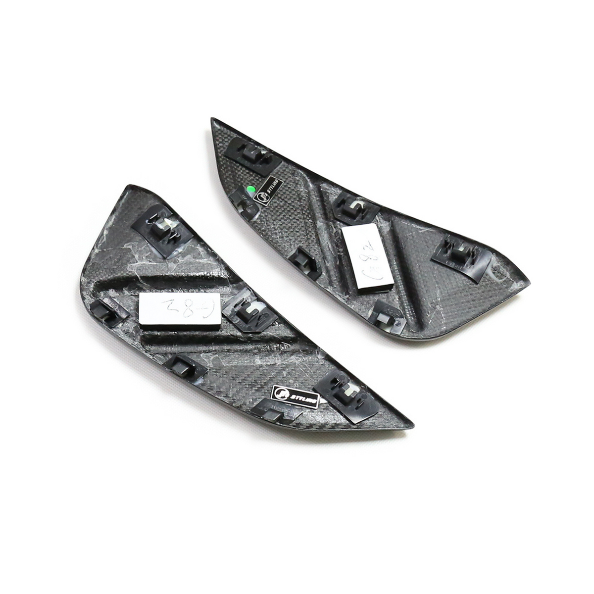 Two black triangular carbon-fiber car parts with clips, lying on a white surface. Labels on each read “L8?” and “L82.” One displays a small logo labeled “OTOSPIRIT.”