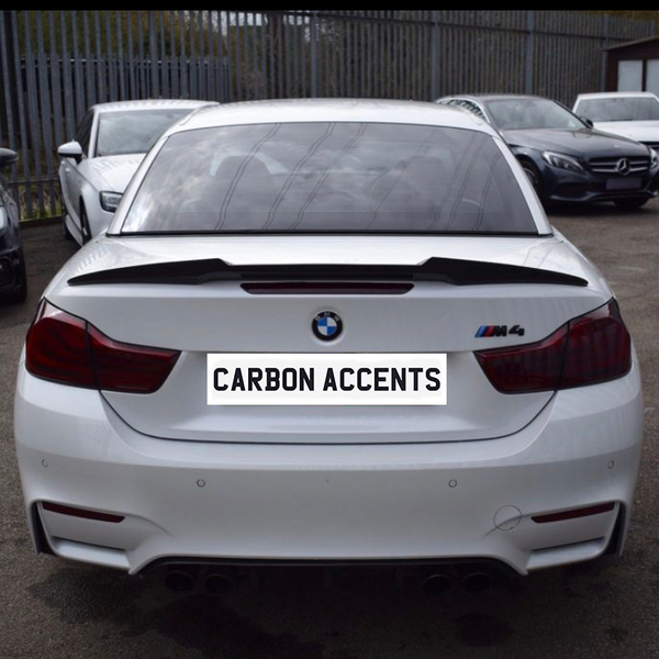 White BMW M4 parked with visible rear carbon accents, in a car lot surrounded by multiple vehicles. License plate reads "CARBON ACCENTS."
