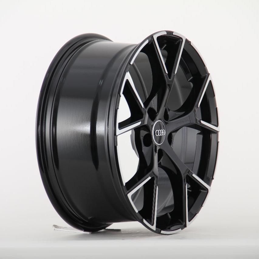 A black alloy wheel with a sleek, silver-accented design is standing upright against a plain white background. The center features a logo with four interlocking rings.