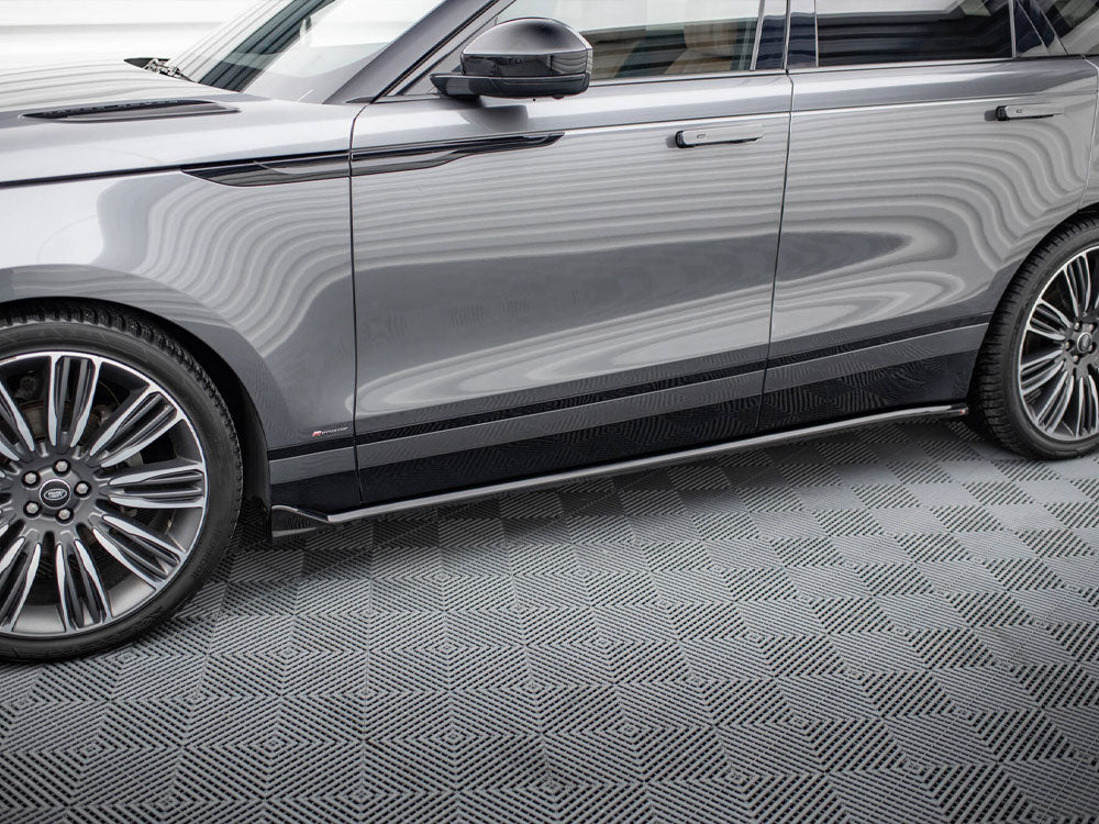 A gray SUV is parked indoors on a patterned floor. The vehicle's shiny surface reflects wavy lines, a black handle is visible, and large chrome wheels dominate the foreground.