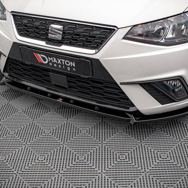 A white car's front end, featuring a black grille and "MAXTON design" text, parked on a patterned grey floor.
