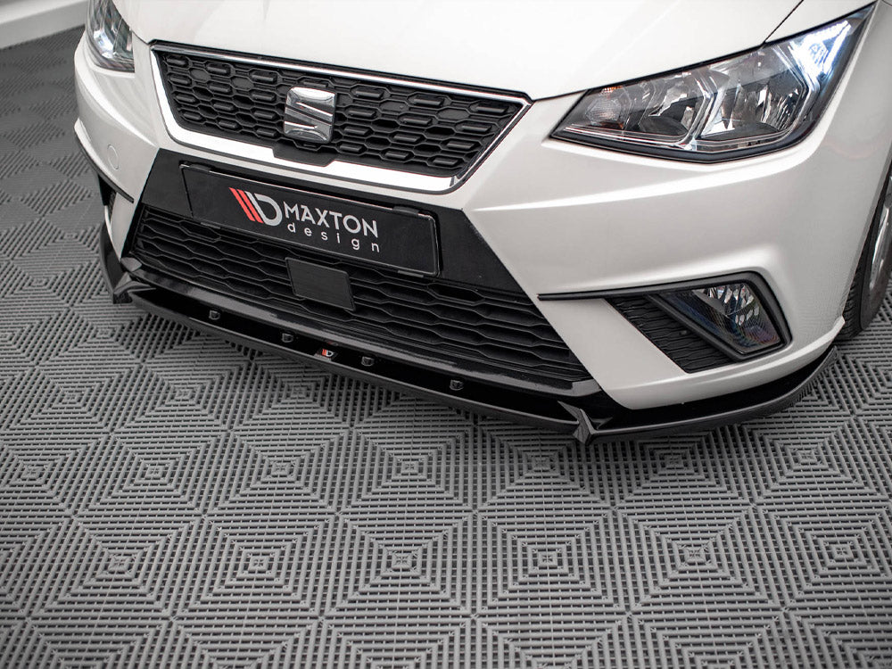 A white car's front end, featuring a black grille and "MAXTON design" text, parked on a patterned grey floor.