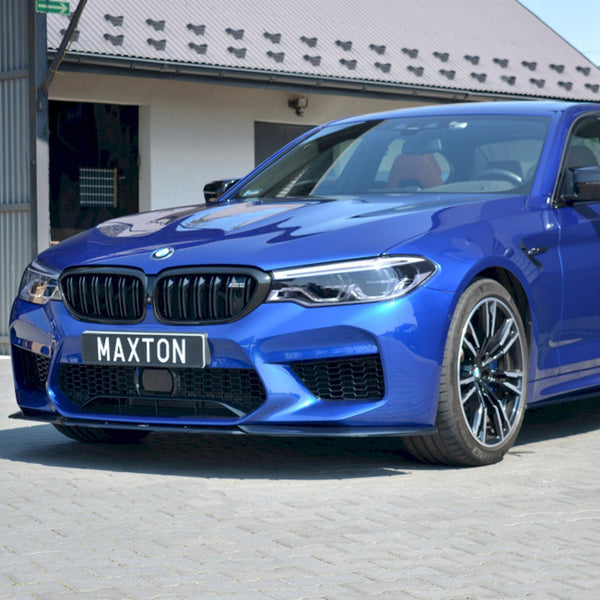 A blue BMW car is parked on a cobblestone surface beside a modern building. The license plate reads "MAXTON."