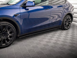 A blue car with black wheels parked in a room with a patterned gray floor and white corrugated walls. The tire reads 