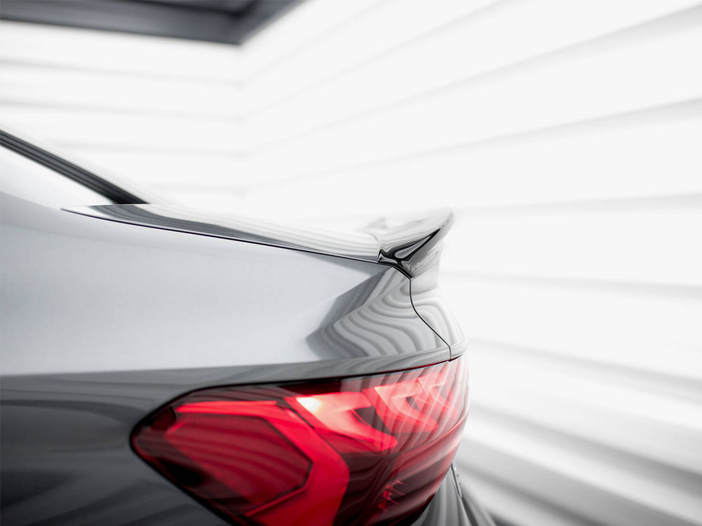 A sleek car's rear with a dark metallic finish and tail light glowing red, parked in a bright, modern, white-paneled environment.