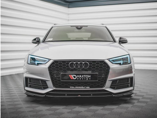 A silver Audi car with illuminated headlights is parked in a tiled, enclosed space. The front license plate reads "MAXTON design" and "quattro" below.