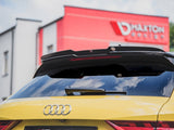 Yellow Audi parked with rear view featuring a spoiler and license plate. Behind, a red building displays the text 