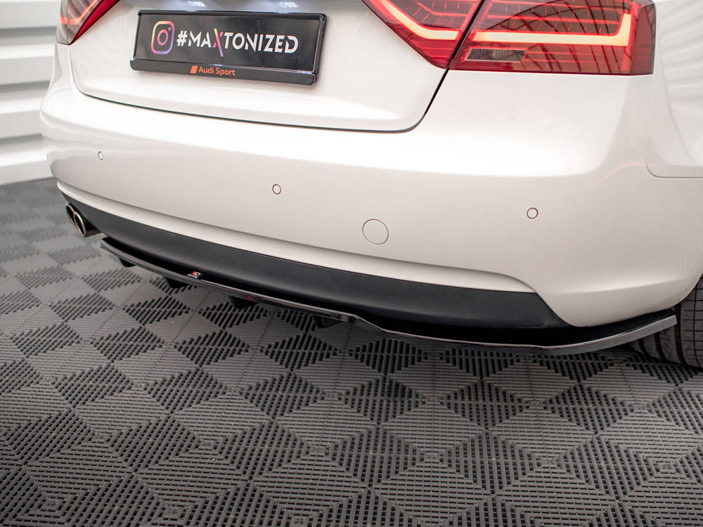 The rear of a white car with a visible black diffuser and dual exhausts, features a "#MAXTONIZED" tag and Audi branding, parked in a garage with checkered flooring.