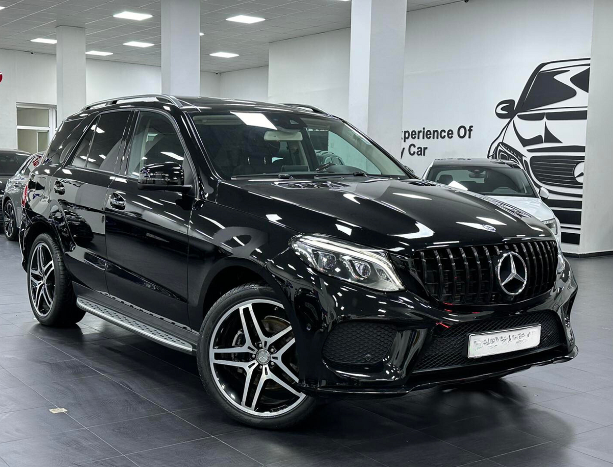 A black SUV is parked indoors, featuring a sleek design and alloy wheels. The setting is a showroom with white walls and a car illustration. Text on the wall reads, "Experience Of Luxury Car."