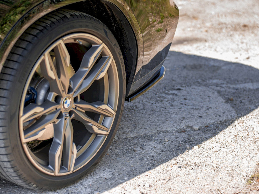 A car tire with a distinctive alloy wheel design is stationary on a rough, sunlit gravel surface, partially casting a shadow. The BMW logo is visible on the hubcap.