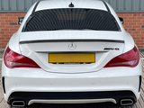 A white Mercedes-Benz AMG car is parked, featuring dual exhausts and tinted windows, against a backdrop of red brick and corrugated metal. Text: 