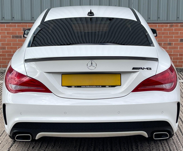 A white Mercedes-Benz AMG car is parked, featuring dual exhausts and tinted windows, against a backdrop of red brick and corrugated metal. Text: "www.mdscarsales.co.uk".